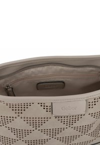 Beige Handtasche mit durchbrochenem Design und glatter Textur. Verfügt über eine Reißverschlusstasche innen und ein tannfarbendes Stofffutter. Gabor-Logo sichtbar.