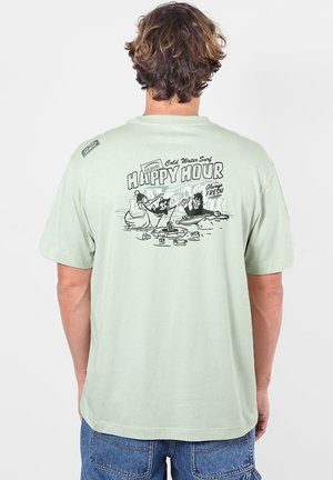 Personne portant un t-shirt vert clair avec un dessin animé noir de deux personnages jouant aux cartes et le texte "Happy Hour" au dos.