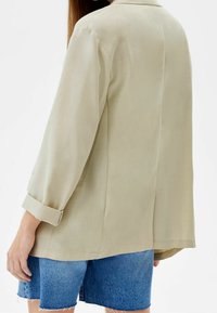 Beige overhemd met lange mouwen en een kraag, opgerolde manchetten en een gladde textuur, gecombineerd met denim shorts. Lichte stof zorgt voor een comfortabele pasvorm.