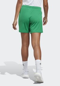 Groene sportshorts met een elastische tailleband, gladde textuur en een ontspannen pasvorm, gecombineerd met witte sokken en lichtgekleurde schoenen.