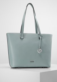 Sac fourre-tout en cuir bleu clair avec deux poignées, bords noirs contrastants et une étiquette argentée avec un logo. Texture lisse, forme rectangulaire.