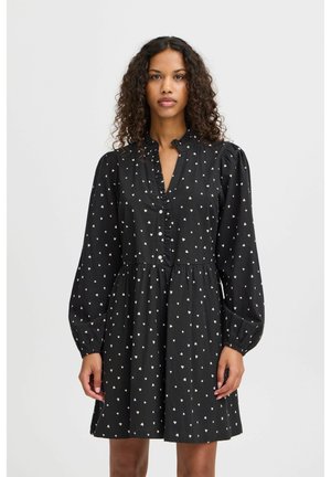 Schwarzes Kleid mit Puffärmeln, Rüschenschenke und Knopfverschluss. Mit kleinen weißen Herzmustern auf strukturiertem Stoff.