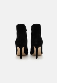 Bottines �à talons hauts noires en daim avec un design ajusté, des fermetures éclair latérales et un talon effilé. Texture lisse avec une finition mate.