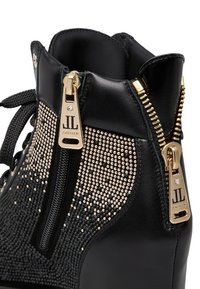 Stivaletto in pelle nera con cerniere dorate e decorazioni con borchie. Caratterizzato da punta tonda, tomaia testurizzata e accenti lucidi.