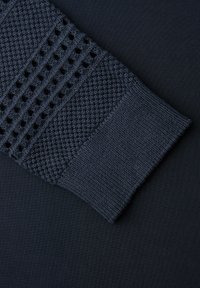 Manica lavorata a maglia blu scuro che mostra tre distinti motivi a trama sul tessuto, su uno sfondo blu scuro uniforme.