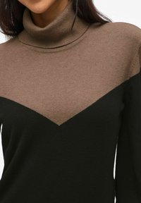 Pull en col roulé avec un motif en blocs de couleurs marron et noir, fini texturé et une couture en forme de V au niveau de la poitrine.