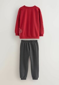 Red sweatshirt with long sleeves and white lettering on the front and sleeve, paired with gray sweatpants featuring ribbed cuffs.