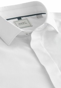 Biała, teksturowana koszula z kołnierzykiem o strukturze, z zapięciem na guziki i przeszywanymi detalami. Metka mówi "NEXT TAILORING."