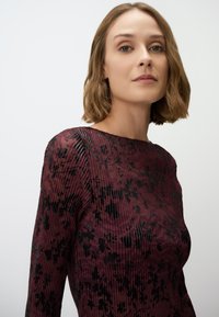 Bordeaux bloemenprint lange mouw jurk gemaakt van textuur stof met sheer accenten en een ronde halslijn.