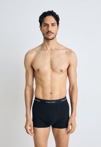 Zwarte katoenen boxershorts van een gladde textuur met een Calvin Klein-logo op de tailleband, getoond op een model tegen een neutrale achtergrond.
