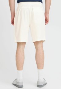 Cream-colored shorts with an elastic waistband, knee-length cut, and a smooth texture, paired with gray sneakers and white socks.