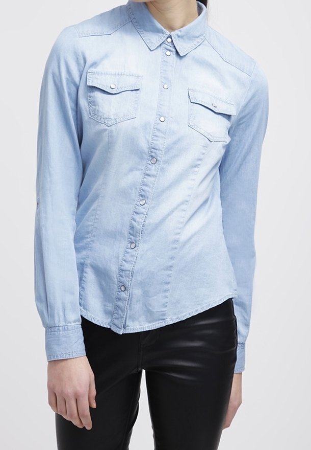 Light blue denim shirt with long sleeves, button-up front, and two chest pockets. Features a classic collar and subtle texture.