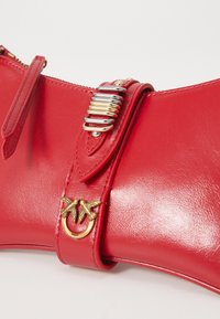 Red leather handbag with a glossy finish, featuring gold hardware, an interlocking bird motif, and a decorative strap with metallic accent.