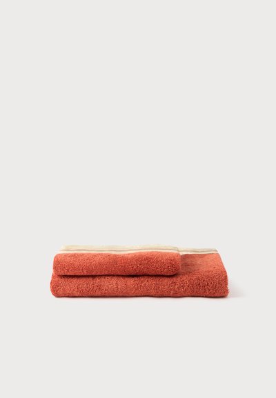 Deux serviettes orange brûlé soigneusement pliées, empilées sur un fond clair, avec une bordure décorative beige sur les bords.