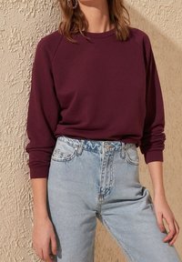 Sudadera burdeos con mangas raglán combinada con vaqueros de cintura alta de un azul claro. Textura suave y corte relajado; el denim cuenta con bolsillos clásicos.