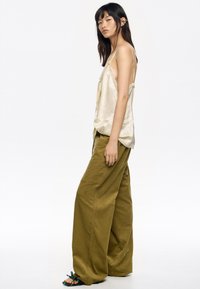 Top de tirantes finos de marfil sedoso, combinado con pantalones anchos de pierna ancha en verde oliva, con un acabado texturizado y bolsillos laterales.