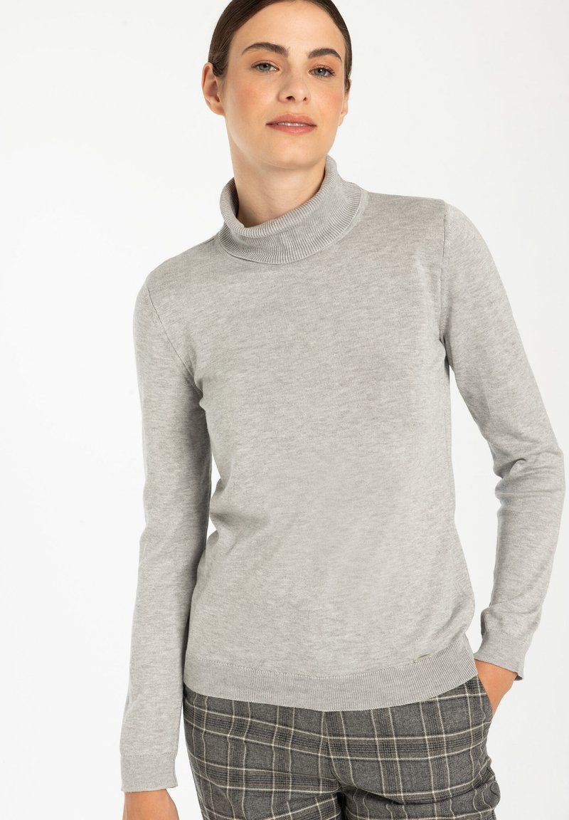 Hellgrauer Rollkragenpullover mit geripptem Kragen und Bündchen, aus weichem Material, kombiniert mit Hosen im Karomuster.