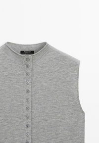 Grå ärmlös cardigan med rund halsringning, med en rad av sex gråa knappar på framsidan. Mjuk stickad textur.