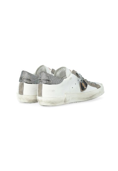 Baskets basses blanches avec des accents en daim gris, des languettes de talon à motifs, des lacets noirs et blancs, et des semelles légèrement usées, orientées vers la droite.