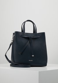 Borsa blu navy in materiale strutturato, con due manici, tracolla removibile e dettaglio fiocco decorativo. Logo del marchio visibile.