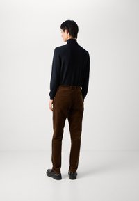 Brune fløjlsbukser med lige pasform, der har en glat tekstur og baglommer, parret med en tætsiddende sort langærmet bluse.
