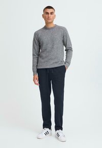 Siv pulover pleten z okroglim izrezom, v kombinaciji z mornarsko modrimi hlačami na vrvico. Model nosi bele superge s črnimi črtami. Preprost, sproščen outfit.