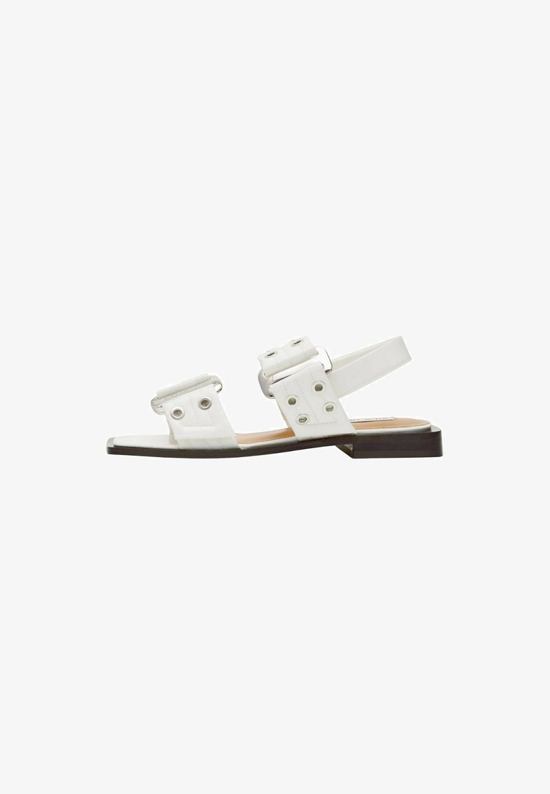 Weiße Sandalen mit zwei breiten Riemen, die kreisförmige Ausschnitte aufweisen, einem Hinterriemen und einem niedrigen braunen Blockabsatz. Glatte Textur und minimalistisches Design.