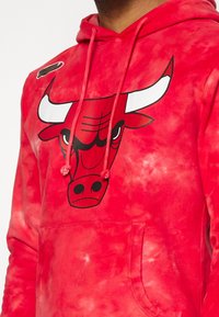 Sweat à capuche tie-dye rouge avec un grand logo des Chicago Bulls représentant une tête de taureau rouge avec des cornes blanches et des yeux noirs sur la poitrine.