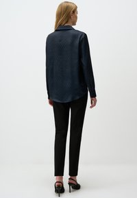 Dark blue patterned long-sleeve blouse with a collar, featuring a lightweight fabric and a curved hem, paired with black fitted pants.