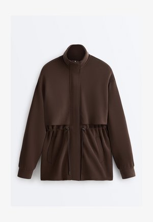 Jachetă maro închis cu mâneci lungi, guler înalt, fermoar frontal, talie cu șnur și două buzunare laterale.