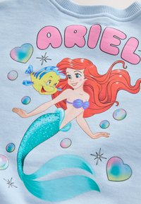 Ariel, la sirena de cabello rojo, nada junto a un pez amarillo y azul con burbujas y corazones pastel sobre un fondo azul claro.