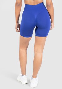 Pantalones cortos deportivos de tiro alto y color azul con un diseño texturizado y silueta ajustada, combinados con zapatillas blancas. Costuras planas y sin logotipos visibles.