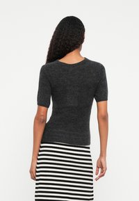 Σκούρο γκρι κοντομάνικο πουλόβερ με υφασμάτινη πλέξη. Διαθέτει στρογγυλή λαιμόκοψη και στενή γραμμή, σε συνδυασμό με μια φούστα σε μαύρο και άσπρο ριγέ σχέδιο.