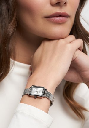 Montre rectangulaire en argent avec un cadran blanc et un bracelet en maille, présentant des index horaires minimalistes et une couronne à 3 heures.