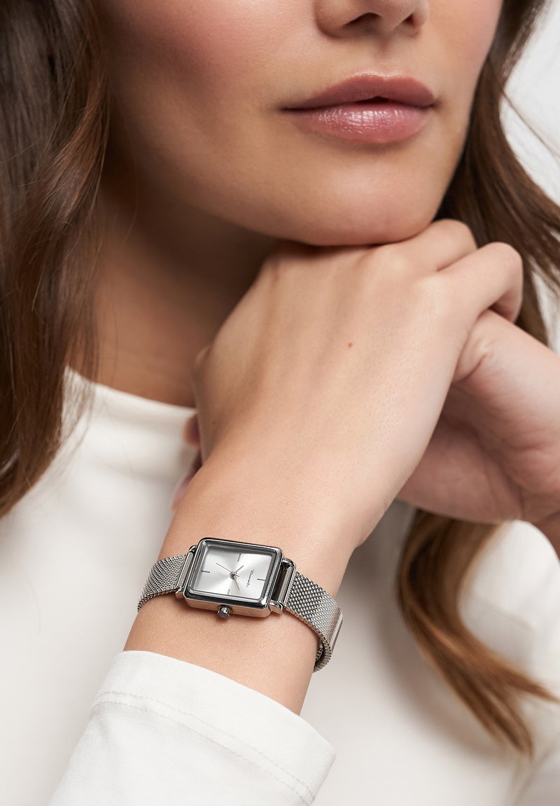 Silberner rechteckiger Uhr mit weißem Ziffernblatt und Mesh-Armband, mit minimalistischen Stundenmarkierungen und einer Krone um 3 Uhr.