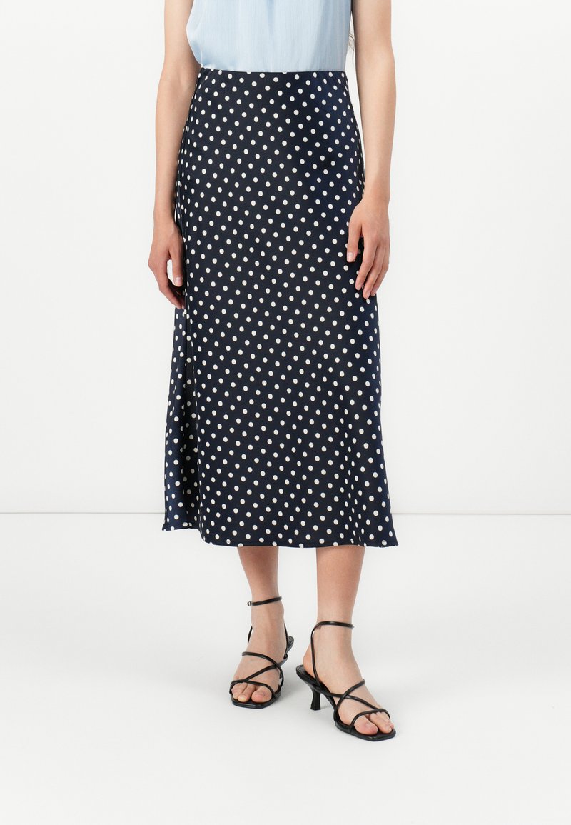 Mørkeblå polkadot midi-skjørt laget av glatt stoff, med en sideslitt og en tettsittende midje. Brukt med svarte stroppeskinn.