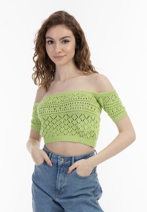 Világos zöld, vállra csúszó, kötött crop top textúrált mintával, rövid ujjakkal és bordázott szegéllyel, magas derekú kék farmernadrággal párosítva.