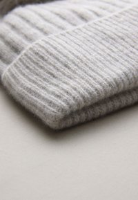 Svetlo sivi pleteni pulover, zložen, s rebrasto teksturo, mehkim volnenim materialom in čisto, preprosto zasnovo brez vidne opreme.