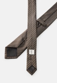 Καφέ ριγέ γραβάτα από λείο ύφασμα, με αιχμηρή άκρη, διακριτική στιλπνότητα και ετικέτα με το όνομα της μάρκας στο στενό άκρο.