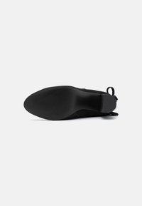 Zapato negro con un upper liso y mate, punta redondeada y suela de goma texturizada. Presenta un pequeño tacón y una lengüeta para facilitar el calzado.