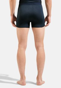Boxers shorts bleu marine en tissu texturé, dotés d'une ceinture élastique ajustée et d'une coupe mi-cuisse. Peau visible sur les jambes.