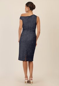 Granatowa sukienka z delikatnym połyskiem, fason bez ramiączek, dopasowany krój, długość do kolan, rozcięcie z tyłu oraz zamek błyskawiczny. Białe szpilki dopełniają wygląd.