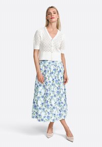 Hvid strikket cardigan med korte puffærmer, parret med en lang, let blå blomsterskirt og nude hæle. Cardiganen har V-udskæring og knapper.