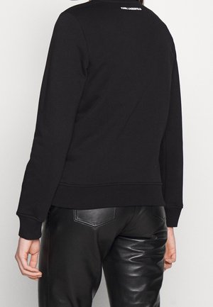 Svart sweatshirt med rund hals och lång ärm, med ribbad kant och muddar. Diskret logotypdetalj på övre delen av ryggen. Matchad med eleganta svarta byxor.