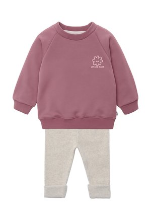 Lila Sweatshirt mit langen Ärmeln und gerippten Bündchen, versehen mit der Blütengrafik "Let Love Bloom", kombiniert mit hellbeigen, hochgekrempelten Hosen.