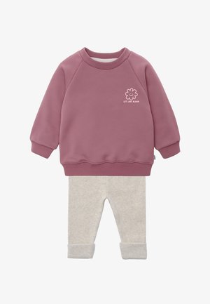 Lila Sweatshirt mit langen Ärmeln und gerippten Bündchen, versehen mit der Blütengrafik "Let Love Bloom", kombiniert mit hellbeigen, hochgekrempelten Hosen.