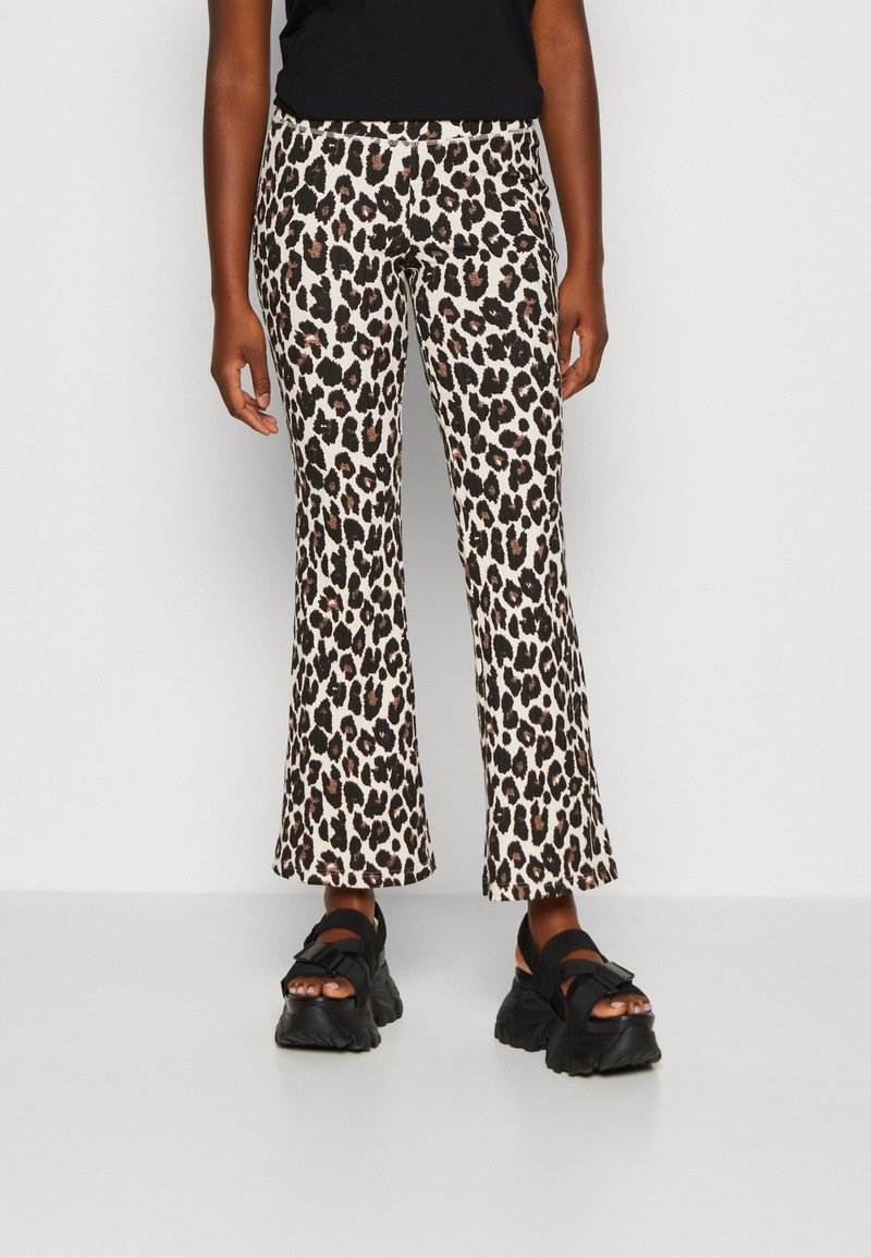 Pantalon évasé à imprimé léopard beige et noir, avec une texture douce. Associé à des sandales noires épaisses à brides.