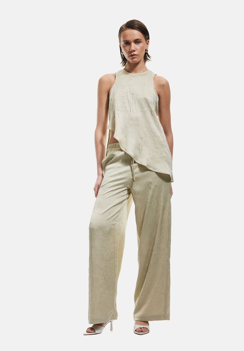 Hellgrünes, strukturiertes Crop-Top mit asymmetrischem Saum, kombiniert mit weiten Hosen aus passendem Stoff. Einfaches Design mit minimalem Zubehör.