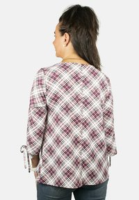 Blusa de cuadros en tonos de púrpura y blanco, con mangas tres cuartos con lazos, detalle en la costura trasera y un ajuste relajado.