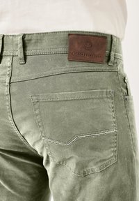 Olivgrüne Hose mit strukturierter Oberfläche, ausgestattet mit einem braunen Lederpatch, das mit "redpoint" beschriftet ist, sowie kontrastierenden Nähten entlang der Taschen.